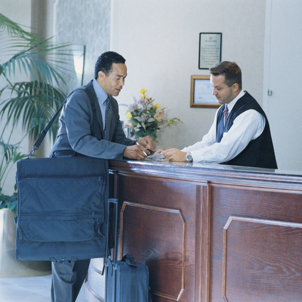 A businessman checks into a hotel at a polished wooden counter, receiving keys from a staff member. Luggage is placed beside him.